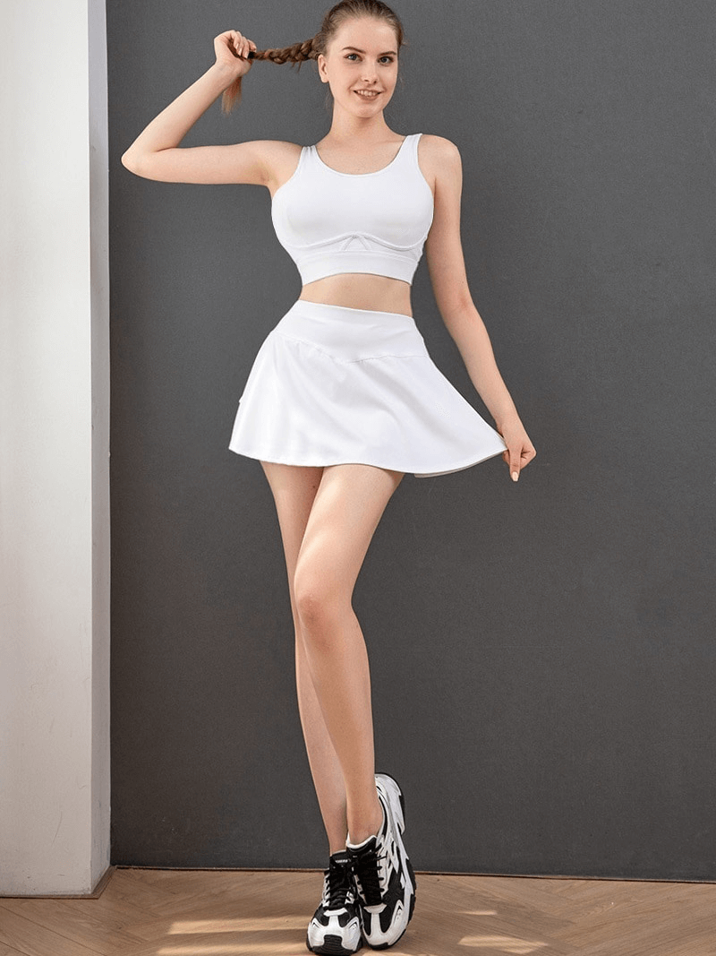 Model wearing white pleated shorts-skirt with inside pocket, ideal for women's golf and tennis, offering comfort and performance.